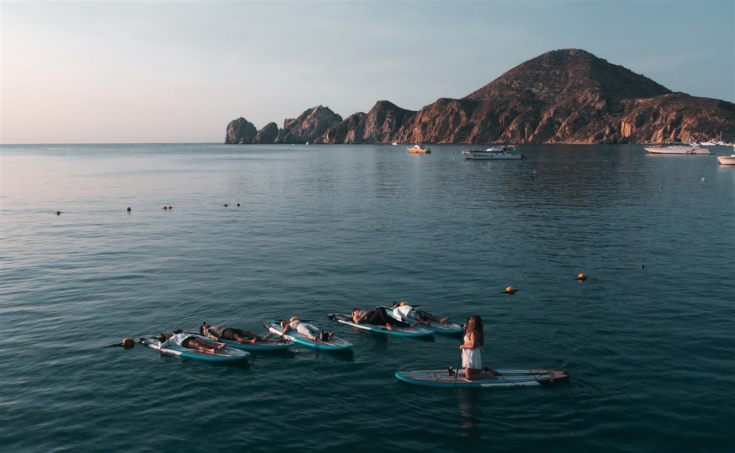 Grupo haciendo yoga sobre las tablas al atardecer, con Lands End al fondo